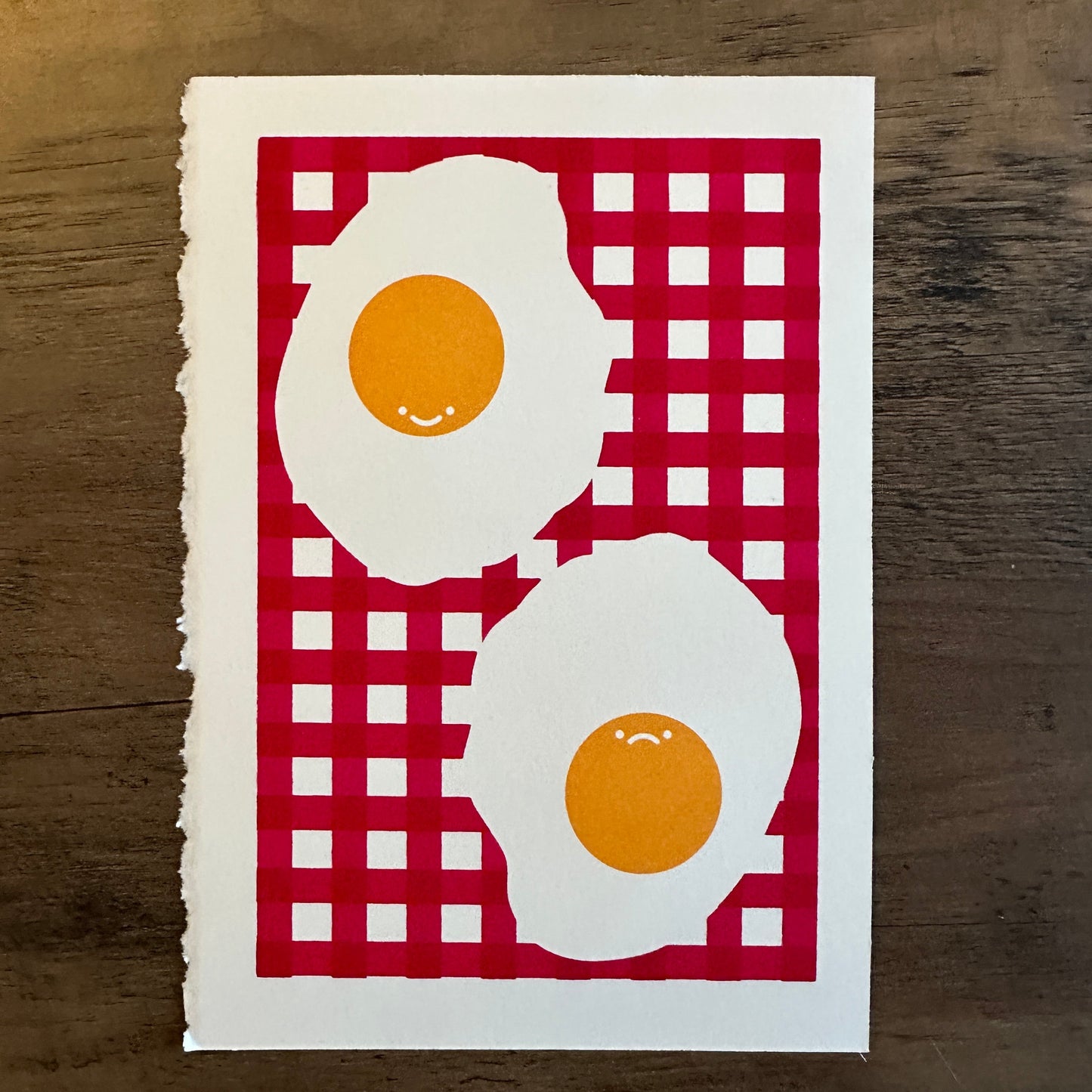 Two fried eggs on a red and white checkered cloth with a wooden background