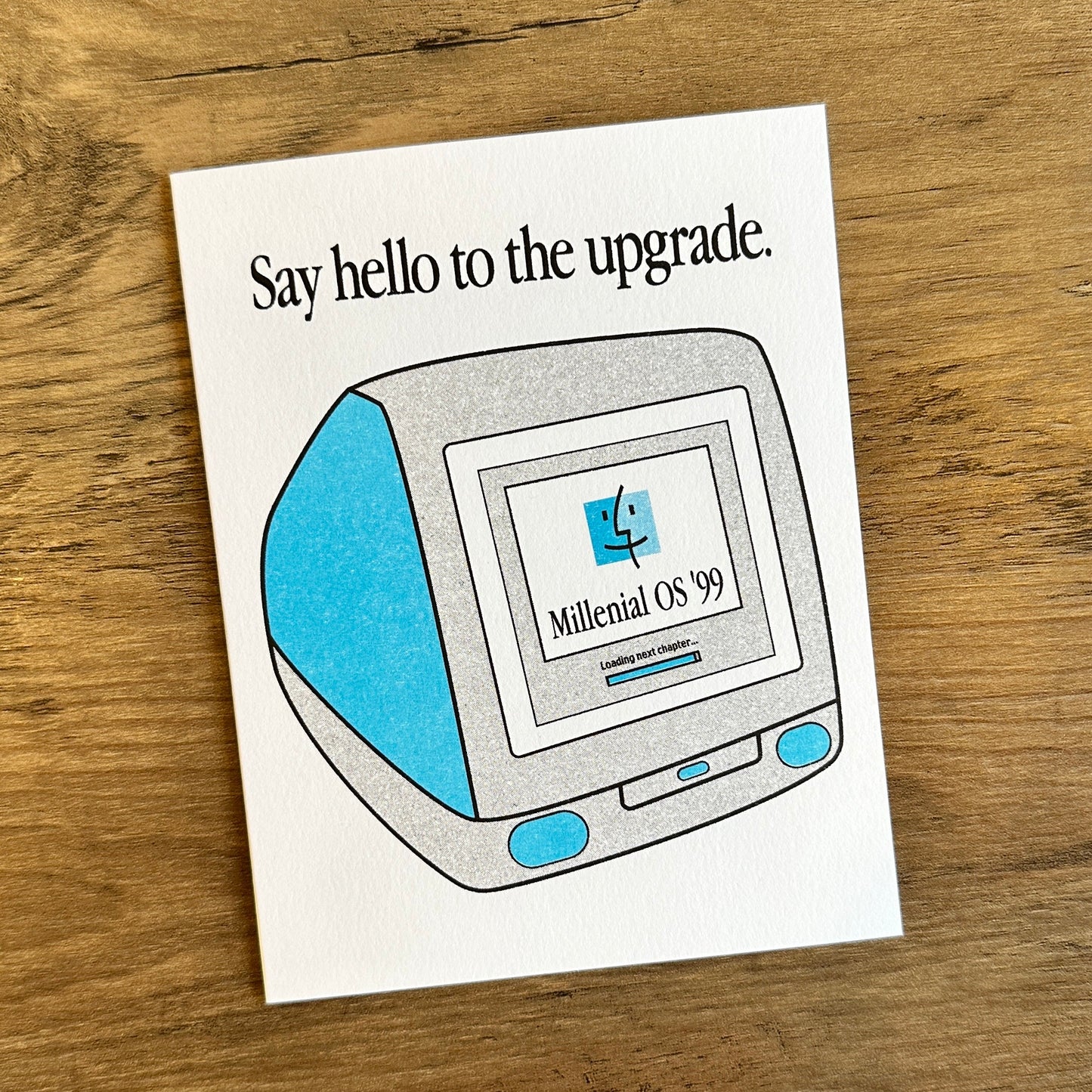 Card with vintage computer design and text 'Say hello to the upgrade.' on a wooden surface